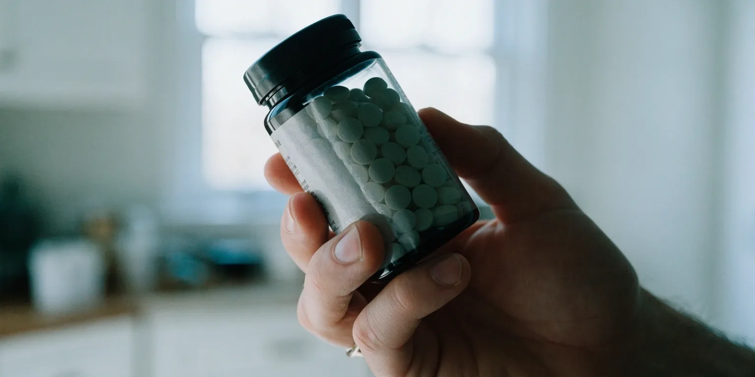 An out-of-focus crop of the back of a supplement bottle on a bright pale counter with the printed panel reduced to soft grey texture