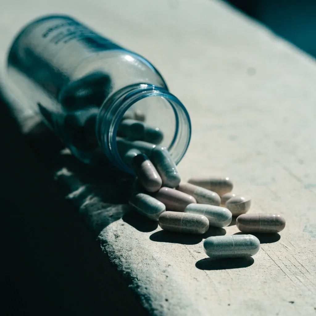Tablets spilling from an open bottle mouth on a bright studio surface